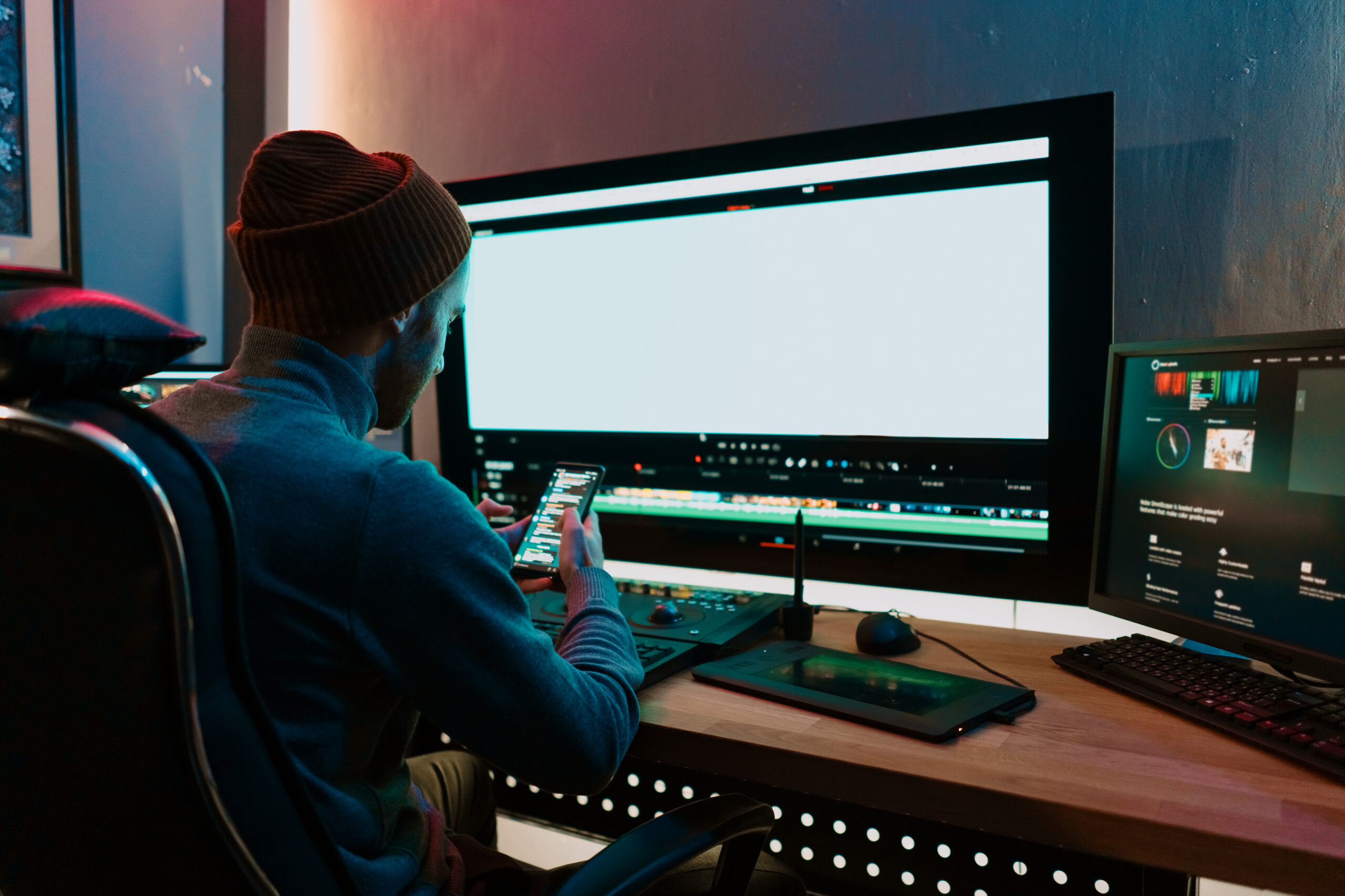 Male Video Editor sitting at his Computer using phone blank screen